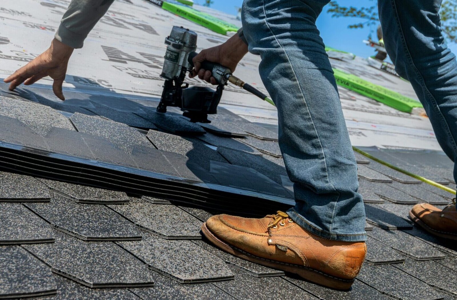 Roofer using nail gun for shingle installation on residential roof.